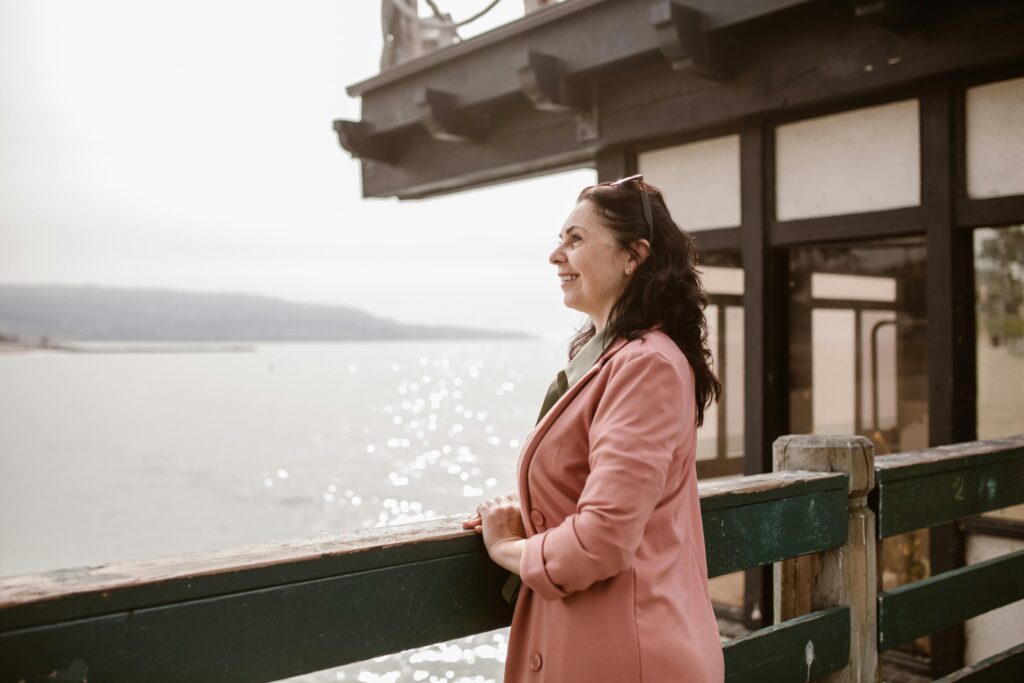 Smiling woman in pink coat enjoying a peaceful moment by the water's edge.